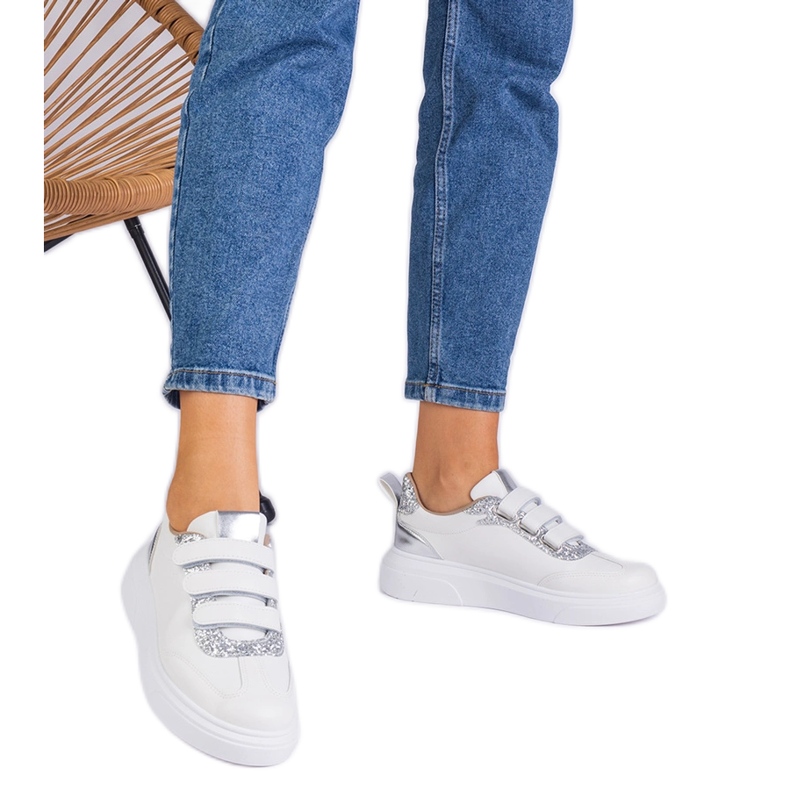 Női fehér és ezüst cipők a tépőzárat csillogóan díszítik Női fehér és ezüst cipők a tépőzárat csillogóan díszítik